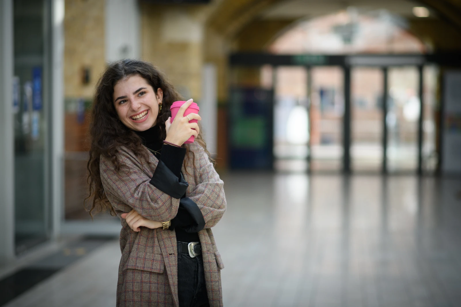 a smiling student in a hallway drinks coffee