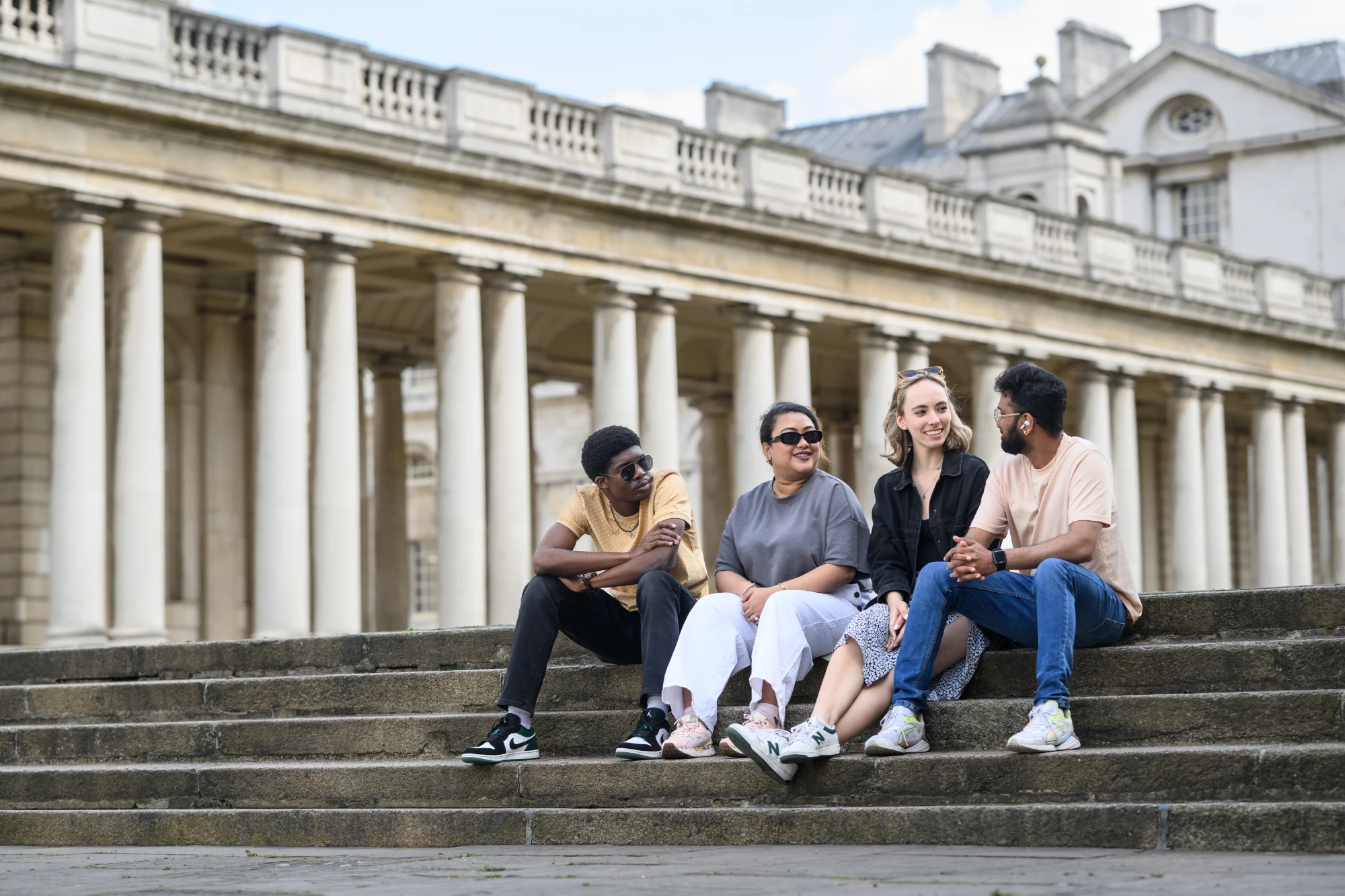 students sitting and laughing on the steps of the royal naval college campus